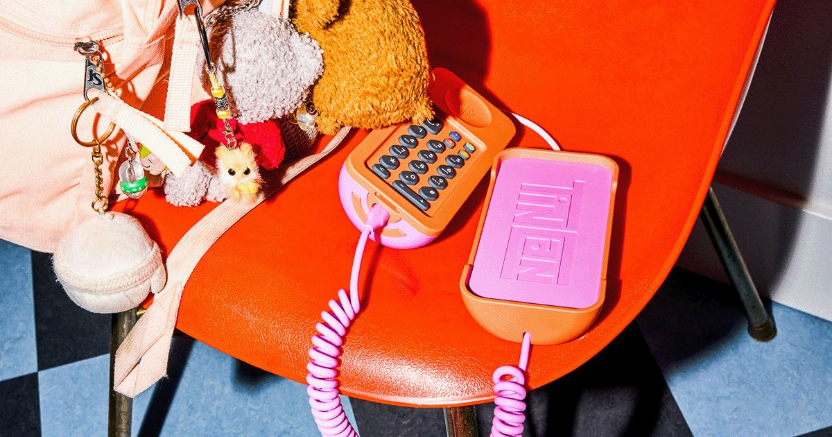 A pink kids' landline with a coiled cord on an orange chair, surrounded by toys