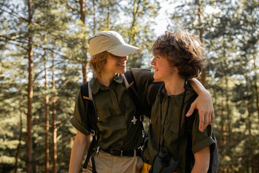 Two kids in hiking gear with their arms around each other in a pine forest